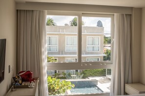 A hotel room with a large window overlooking a pool and a building with multiple windows. - Paraíso Noronha (Fernando de Noronha)