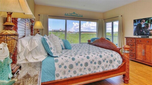 Quarto com cama grande, televisão e vista para o exterior.
