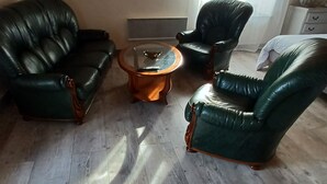 Una sala de estar con dos sofás de cuero verde, una mesa de centro de madera y un espejo redondo en la pared.