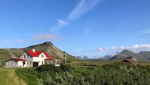 A house with a red roof and a flagpole in a rural setting with mountains in the background. - Suður-Bár Guesthouse (Grundarfjörður)