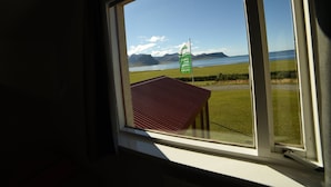 A window with a view of a grassy field, a red-roofed building, and a flag. - Suður-Bár Guesthouse (Grundarfjörður)
