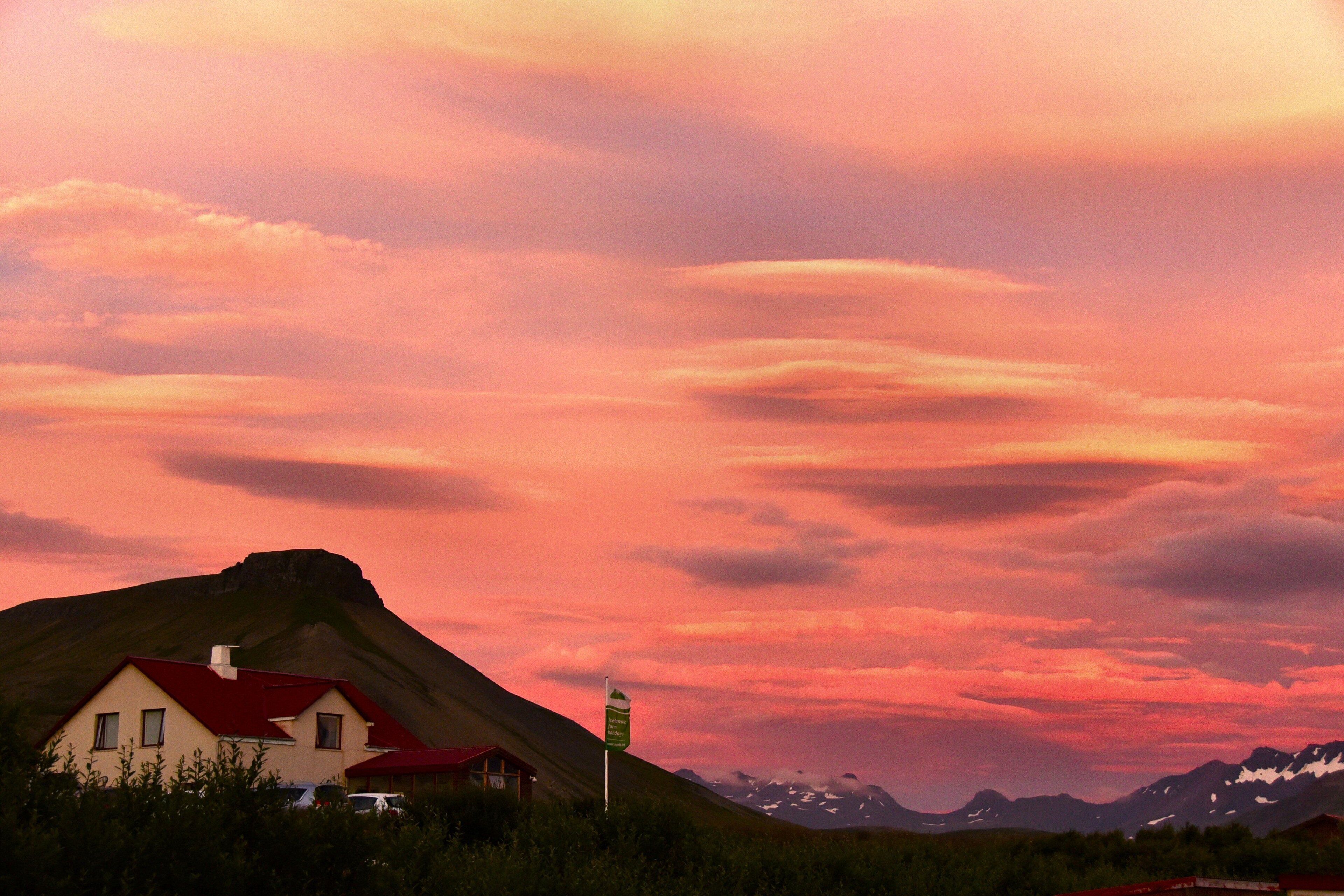 A house with a red roof, a signpost, and a mountainous landscape in the background.
