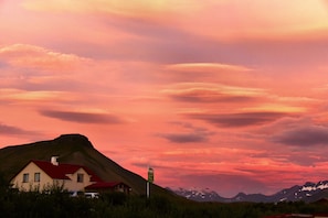 Een huis met een rood dak, een richtingwijzer en een bergachtig landschap op de achtergrond.
