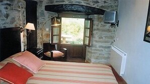 Een slaapkamer met een bed, een stoel, een lamp, een televisie en een raam.