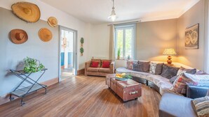 Un salon avec un canapé, une petite table sur laquelle se trouvent des fruits, une valise et une plante posée sur un chariot.