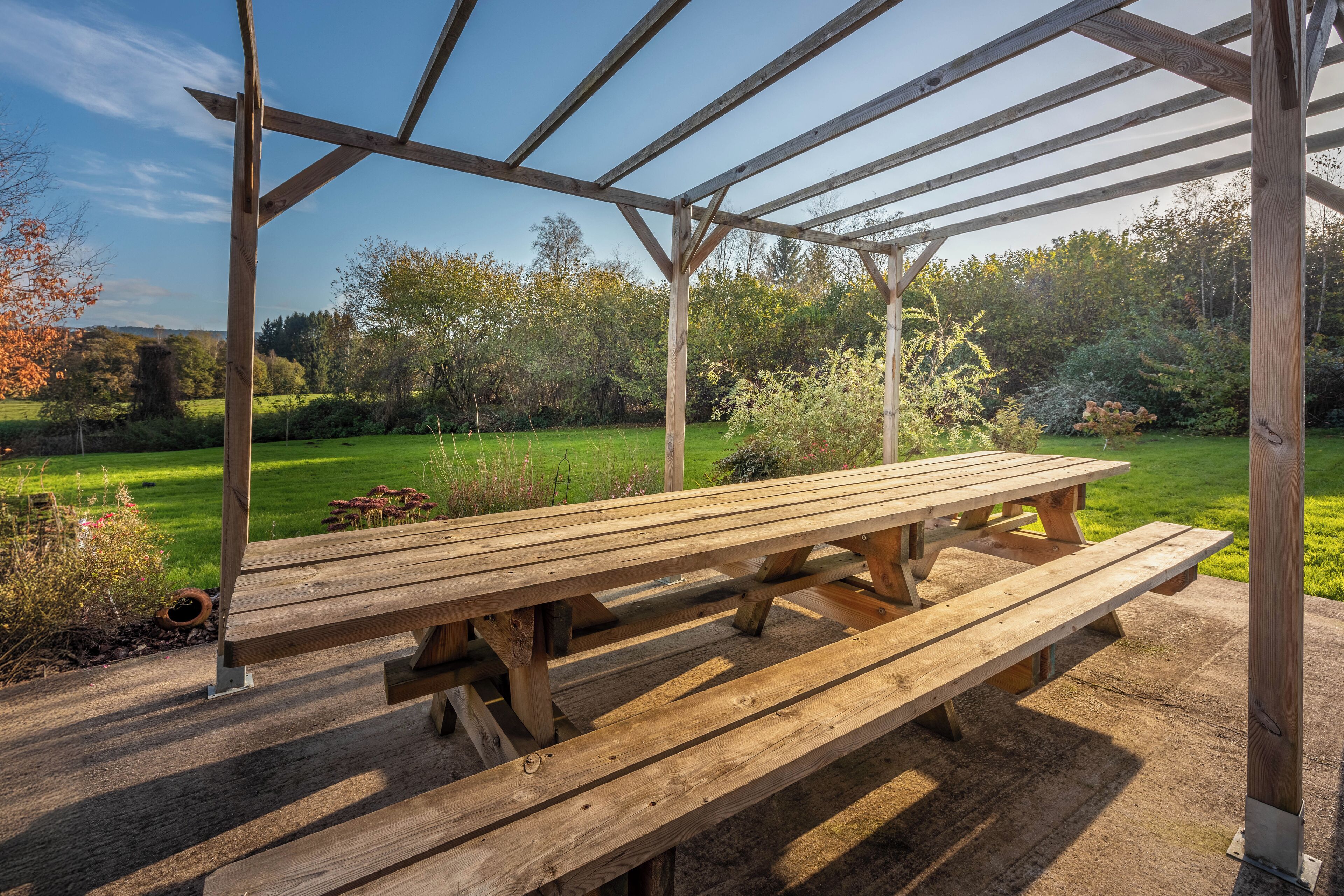 Une pergola en bois avec une table de pique-nique, située dans un jardin.