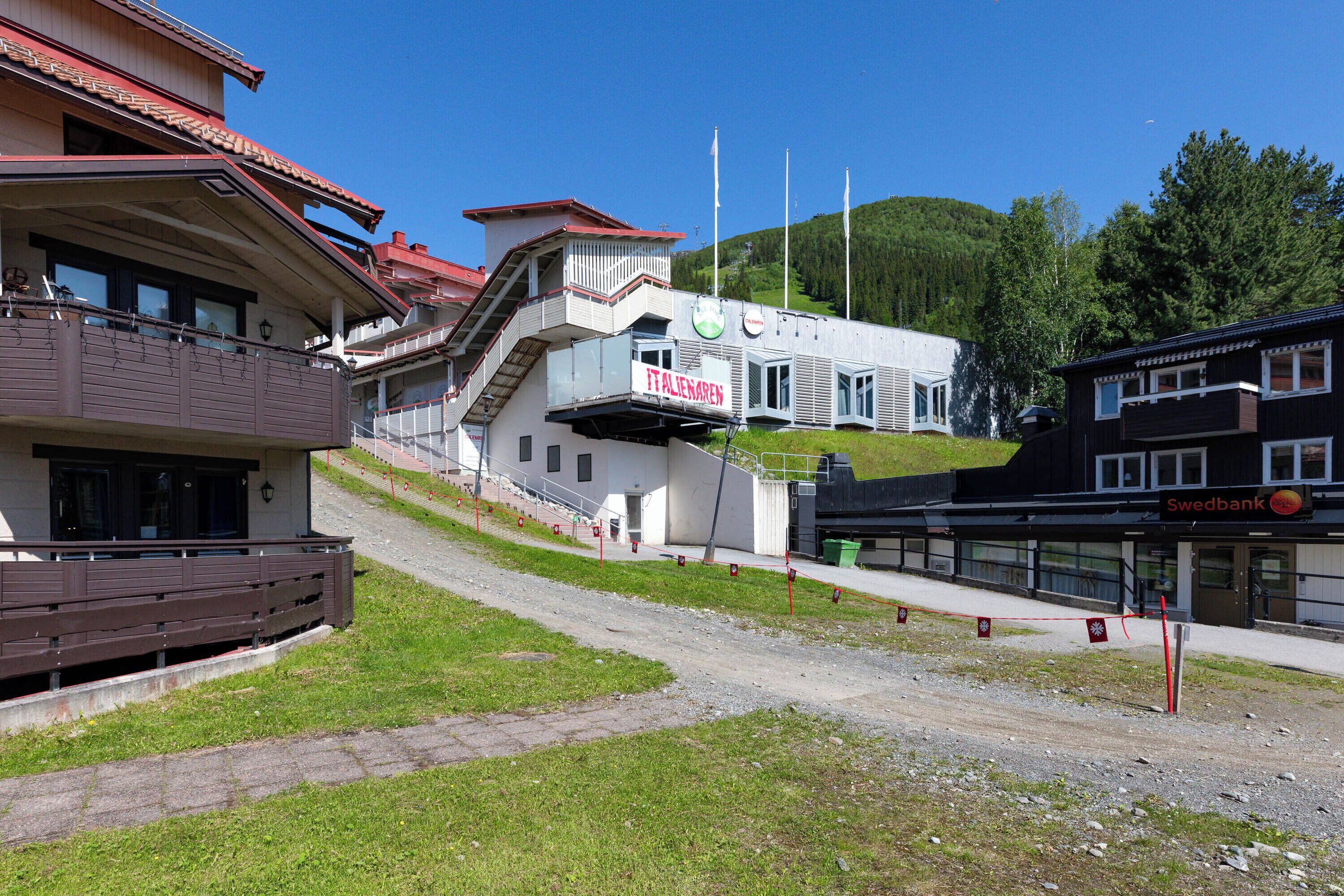 A hotel with a red sign, a staircase leading to a second floor, and a Swedbank sign on the building.