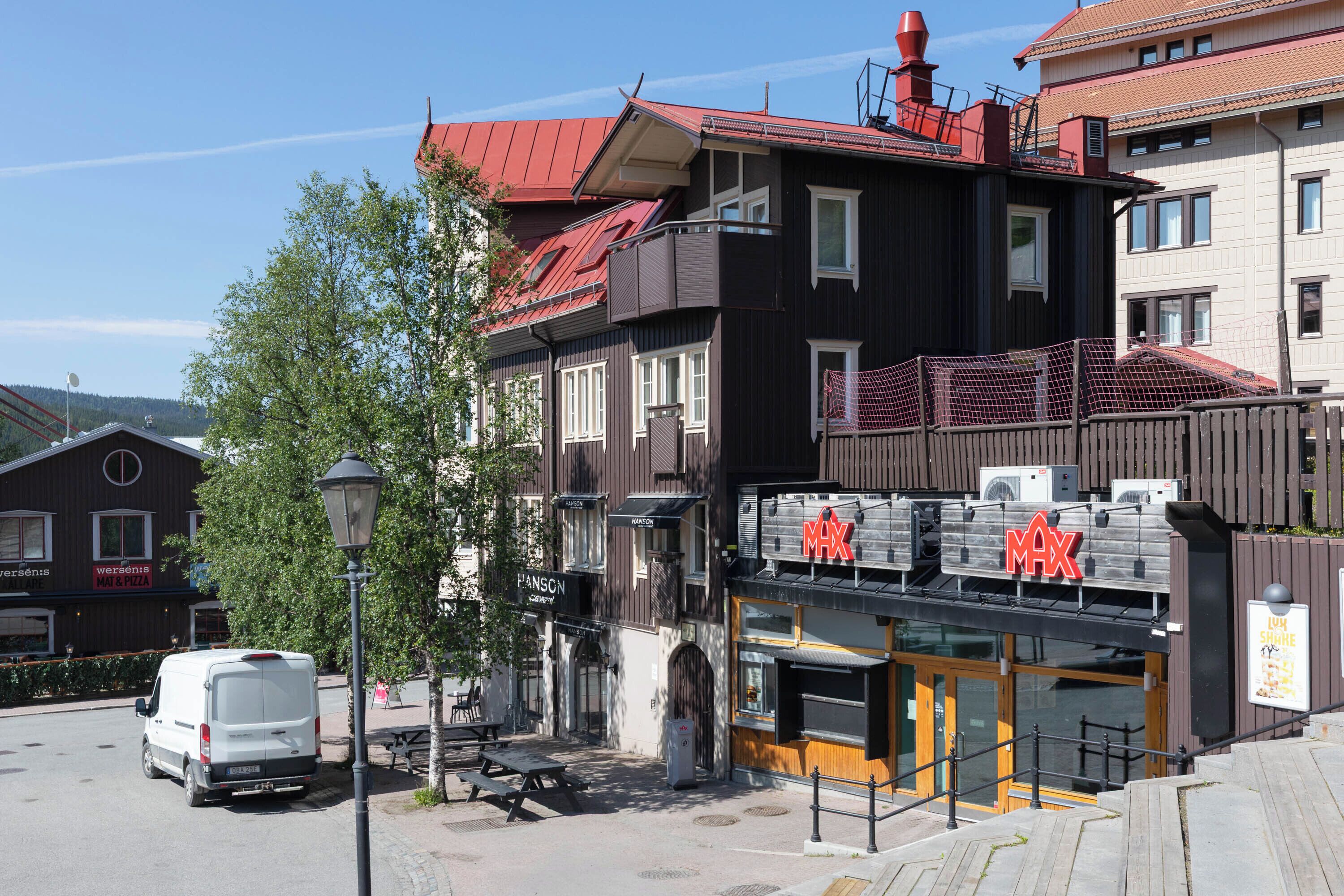 A MAX restaurant with a red roof and a black and white facade, located on a street with a white van parked nearby.