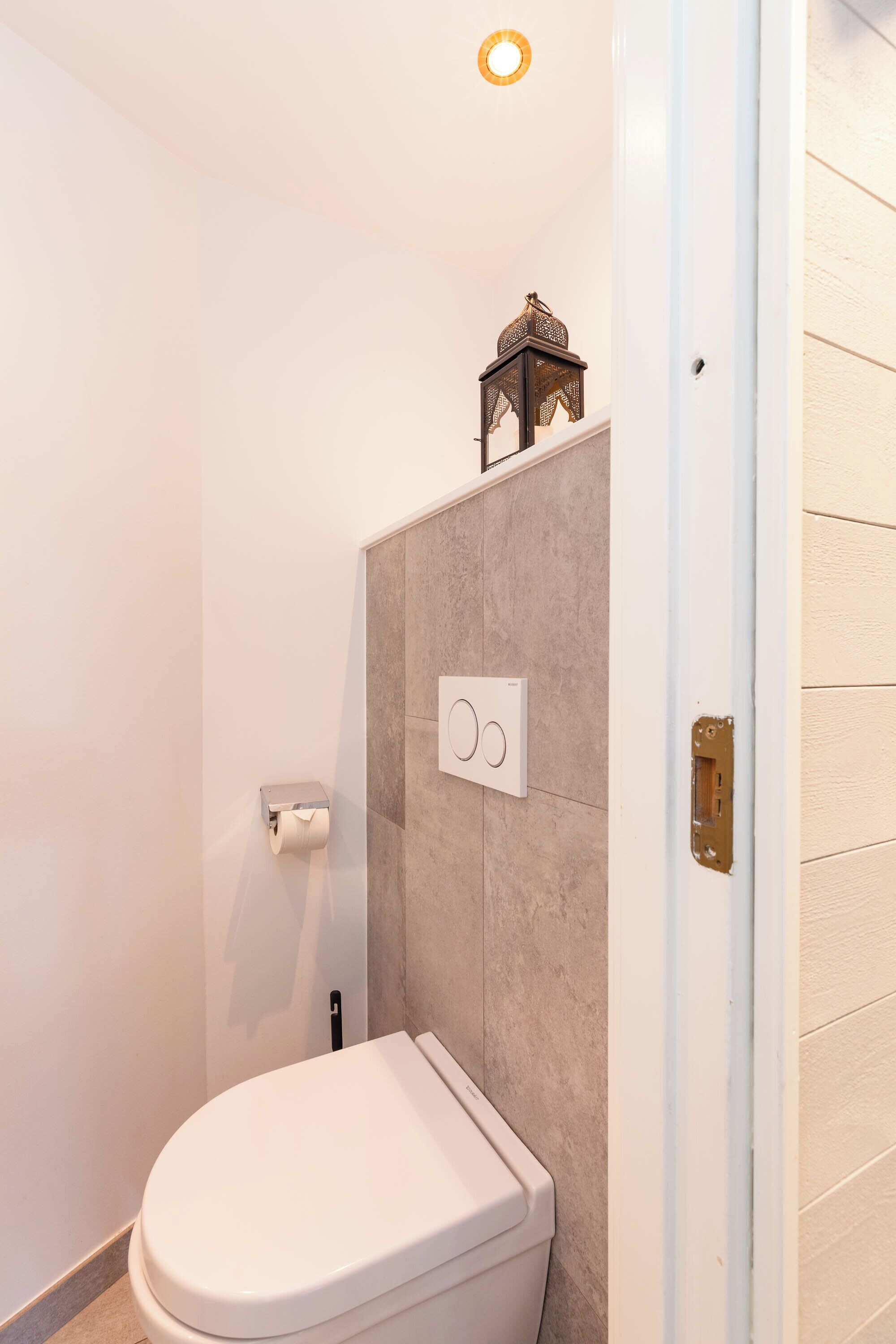 A bathroom with a toilet, a wall-mounted flush handle, a toilet paper holder, and a small decorative lantern.