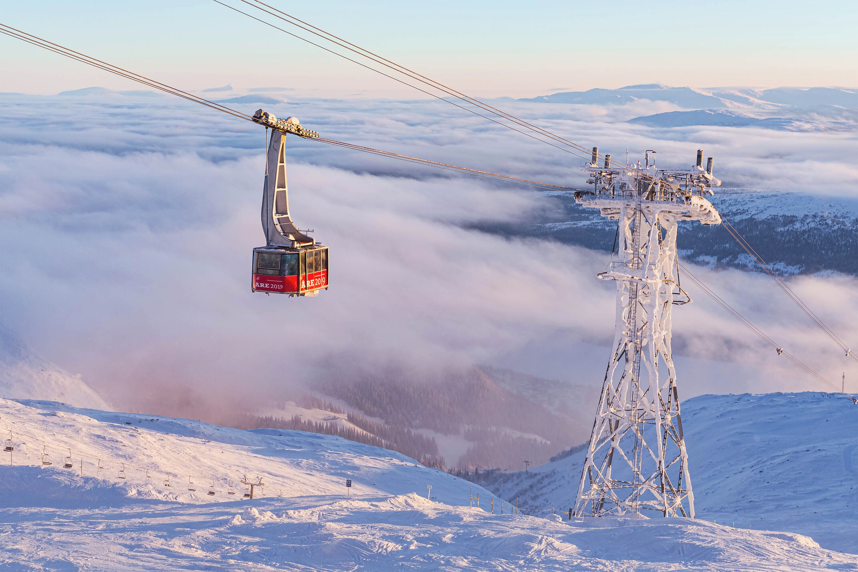 A cable car system with a red cabin, a snowy mountain landscape, and a power pylon.