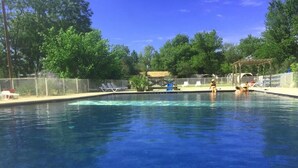 A clear swimming pool surrounded by a fenced area with lounge chairs and a shaded structure.