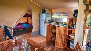 A compact RV kitchen with a refrigerator, microwave, and stove. There is a dining area with a table set for two, and a bunk bed with purple bedding.