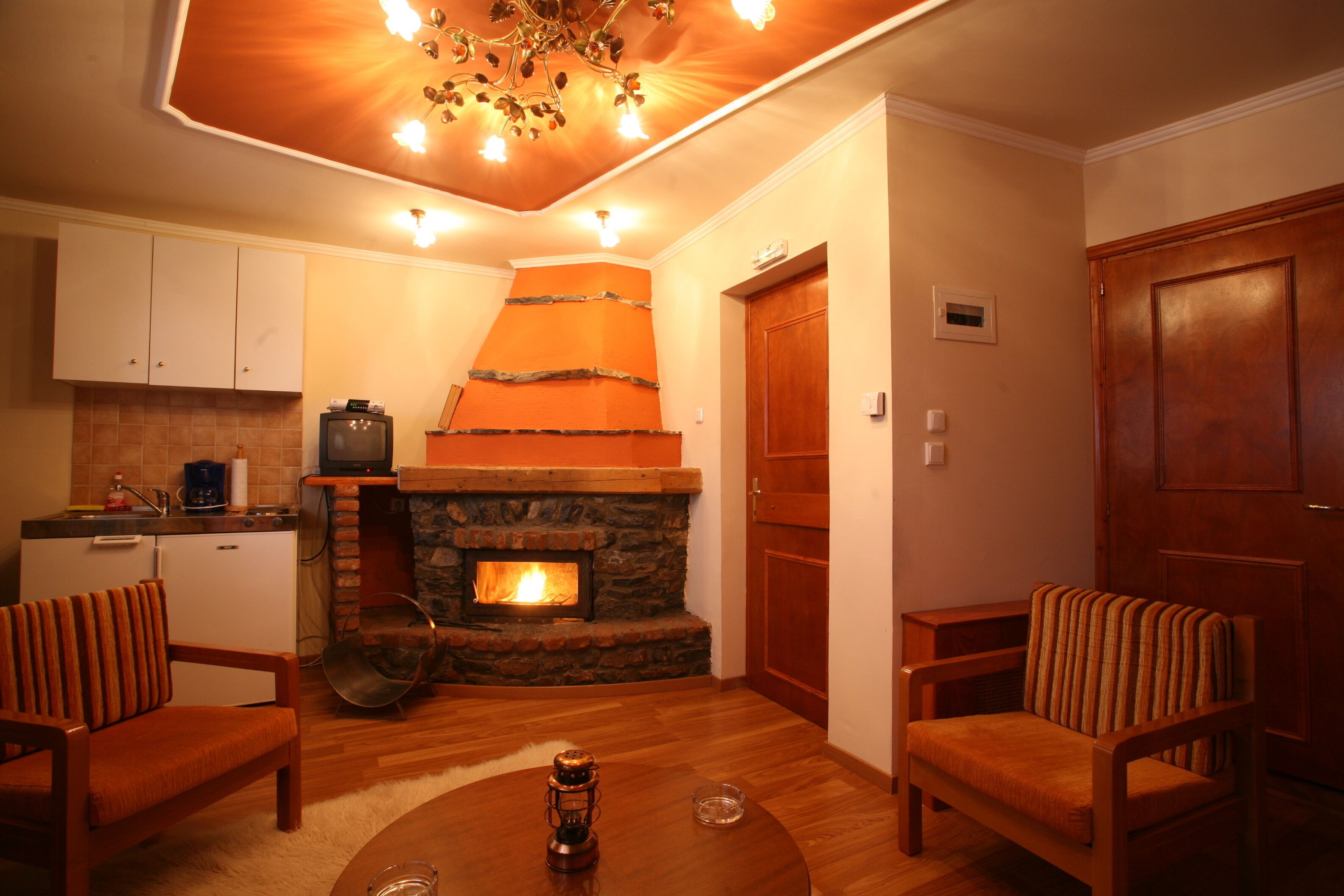 A cozy living room with a fireplace, wooden furniture, and a kitchen area in the background.