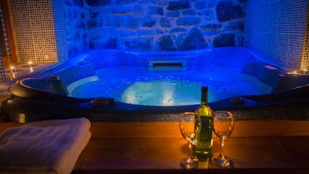 A stone-walled hot tub with a wooden bench and two lit candles. - Exohiko Palaios Agios Athanasios (Edessa)