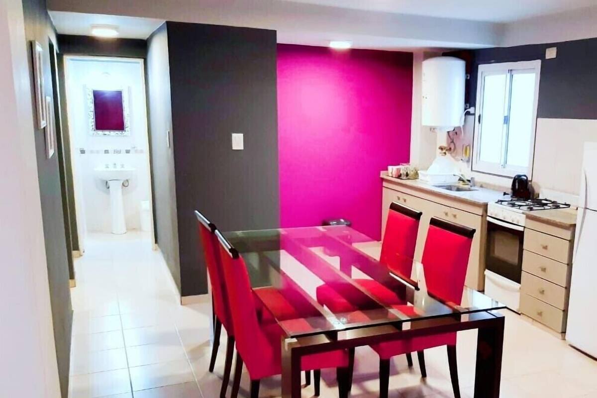 A dining area with a glass table and red chairs, a kitchen with a gas stove, and a bathroom with a white sink.