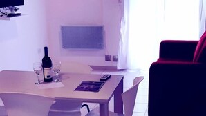 A room with a dining table, a bottle of wine, and glasses, a red chair, and a TV mounted on the wall.