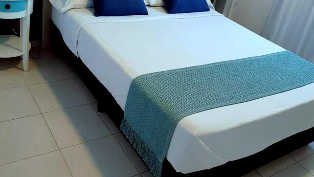 A neatly made bed with a tufted headboard, two pillows, and a teal throw blanket.