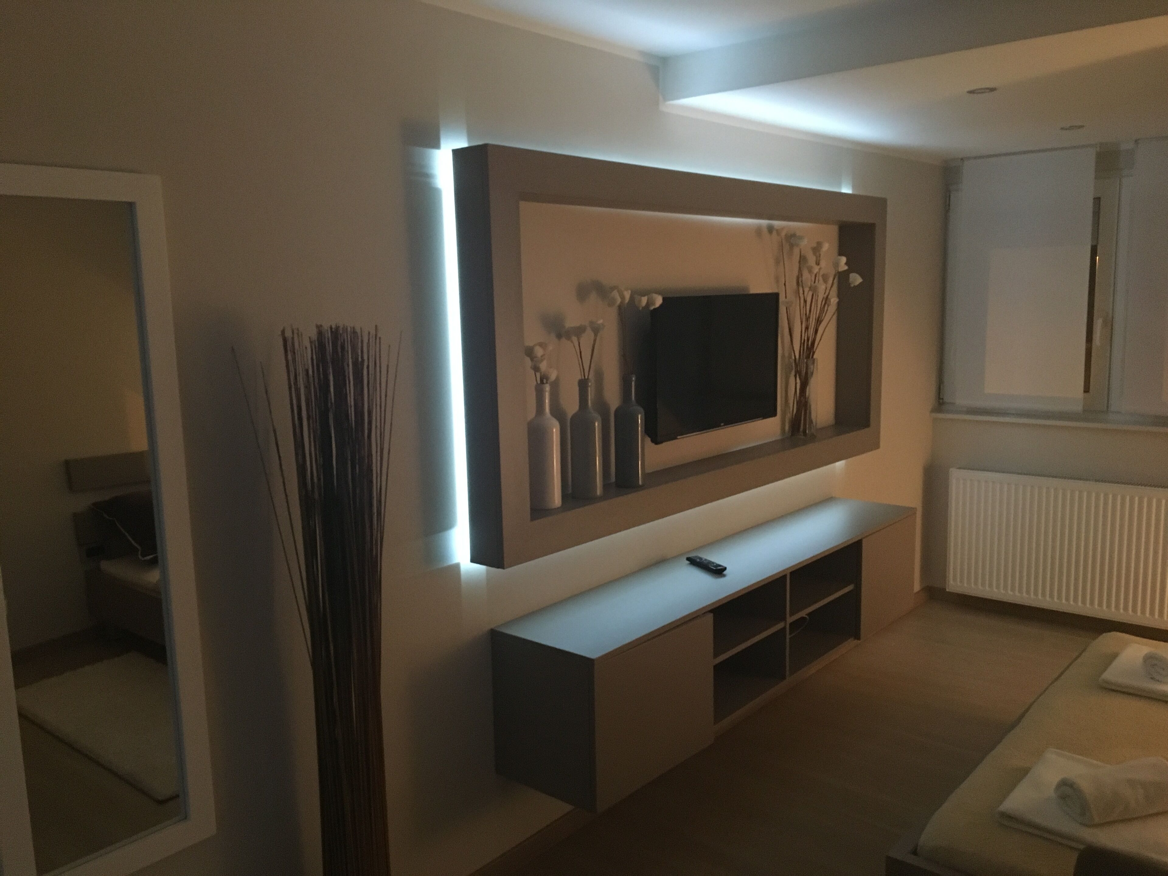Un salon moderne avec un téléviseur à écran plat fixé au mur, une console blanche en dessous et un grand vase décoratif placé sur la gauche.