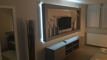 Un salon moderne avec un téléviseur à écran plat fixé au mur, une console blanche en dessous et un grand vase décoratif placé sur la gauche.