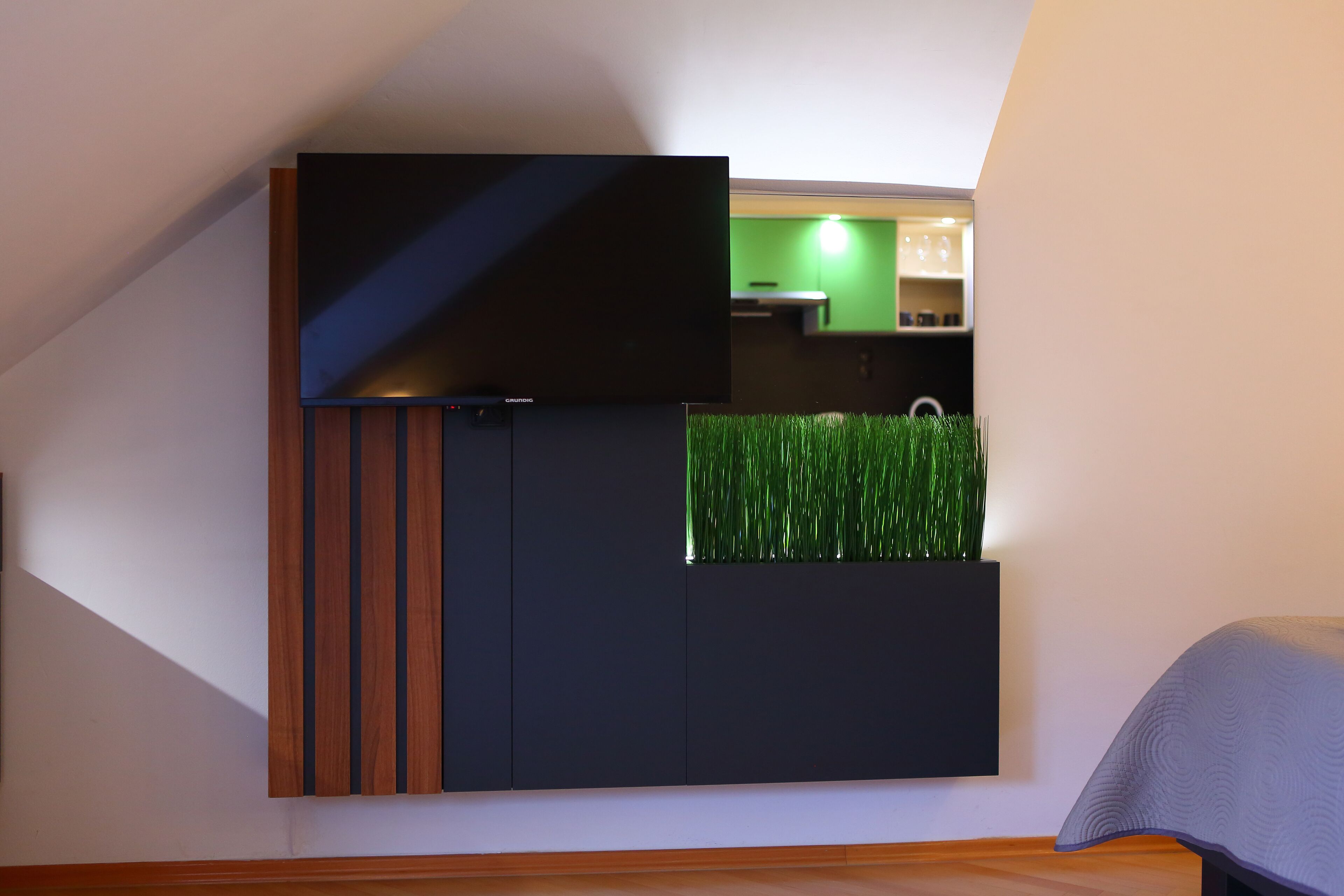 Una habitación moderna con un mueble empotrado para entretenimiento, una pequeña planta verde y una zona de cocina visible al fondo.