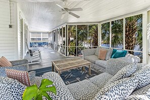 A covered outdoor seating area with patterned furniture, a ceiling fan, and a view of palm trees.