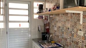 Eine kleine Küche mit Kühlschrank, Herd, Mikrowelle und einem Fenster, inklusive Kaffeemaschine.