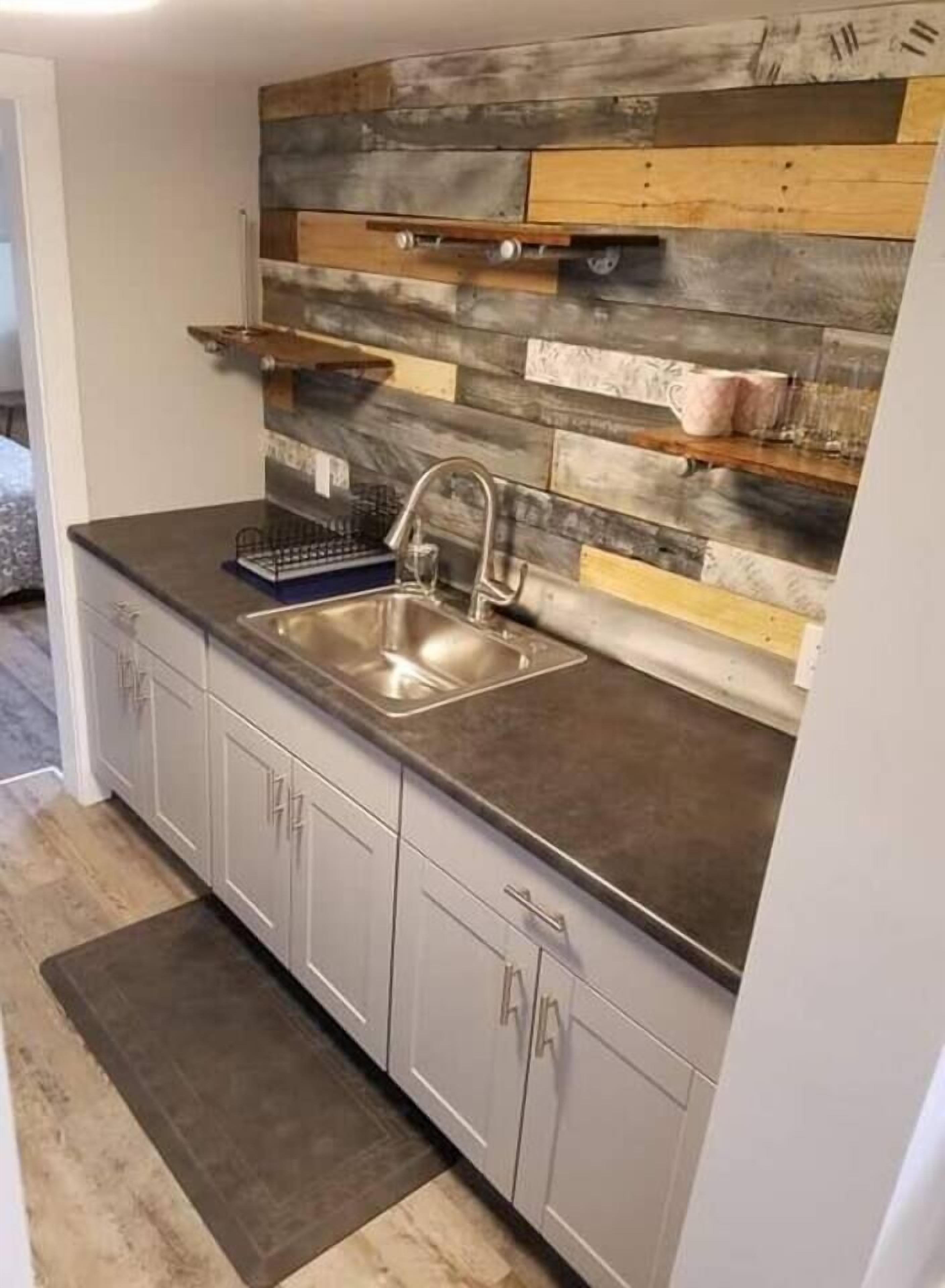 Eine Küche mit modernem Design, ausgestattet mit einer grauen Arbeitsplatte, einer Edelstahl-Spüle und einer Holz-Spritzschutzwand.