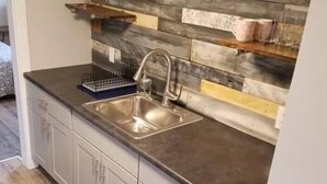 Et køkken med moderne design, grå bordplade, stålvask og træbeklædt væg.
