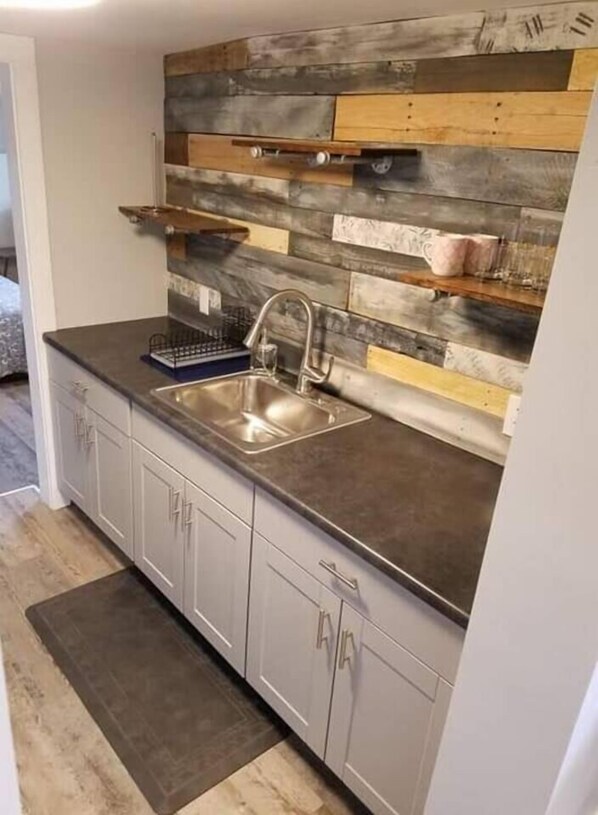 A kitchen with a modern design, featuring a grey countertop, stainless steel sink, and wooden backsplash.