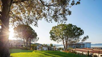 A hotel with a grassy lawn, large trees, and a view of a body of water.