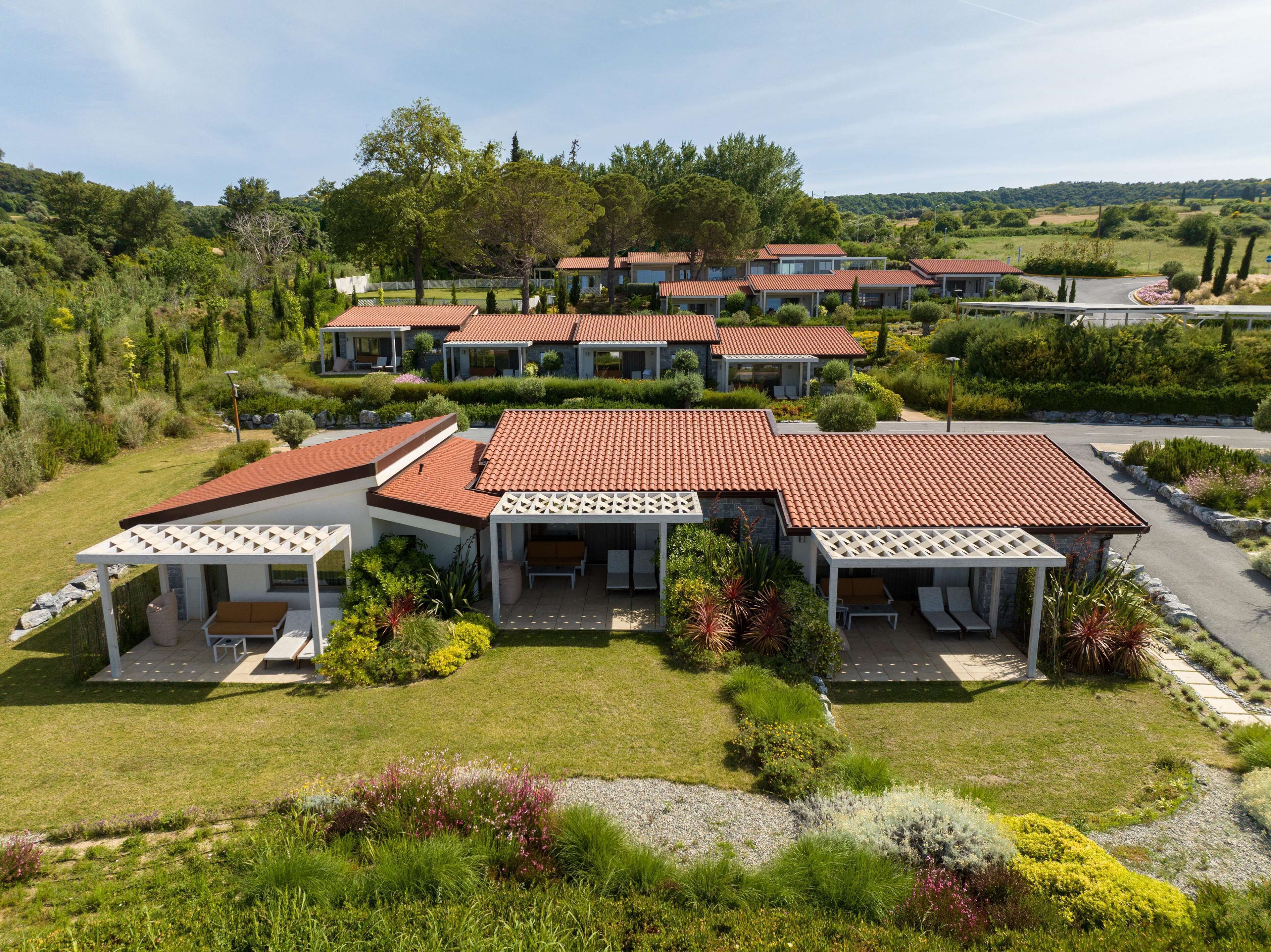 A residential complex with multiple houses featuring red-tiled roofs, white lattice-covered porches, and well-maintained gardens.