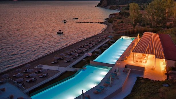 Un resort con zona de piscina, sillones de descanso y vistas al mar al atardecer.