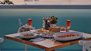 Una mesa lista para comer, con vista al mar y barcos al fondo.