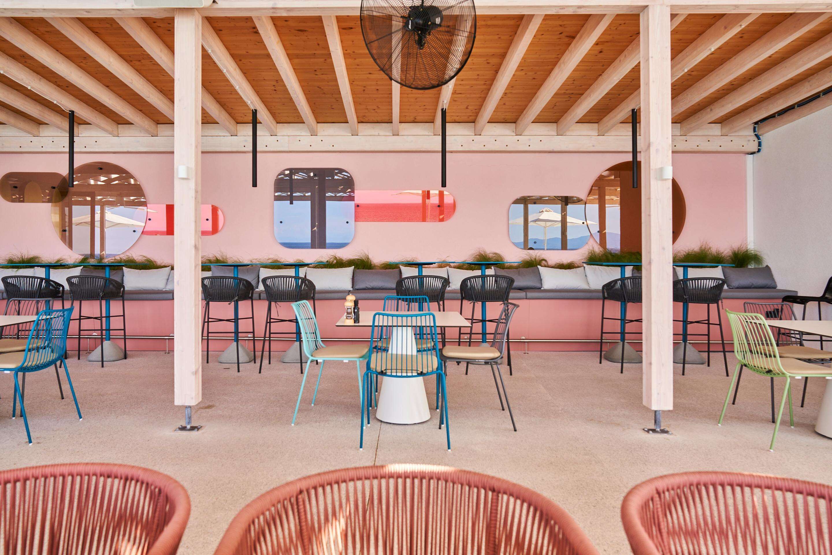An outdoor cafe with wooden beams, round tables, and chairs with various colors.