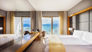 Habitación de hotel con una cama grande, un escritorio con silla, vista al mar y un diseño moderno.
