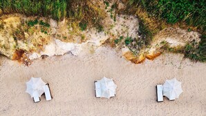 Vista aérea de una playa con tres sombrillas blancas alineadas en la arena.