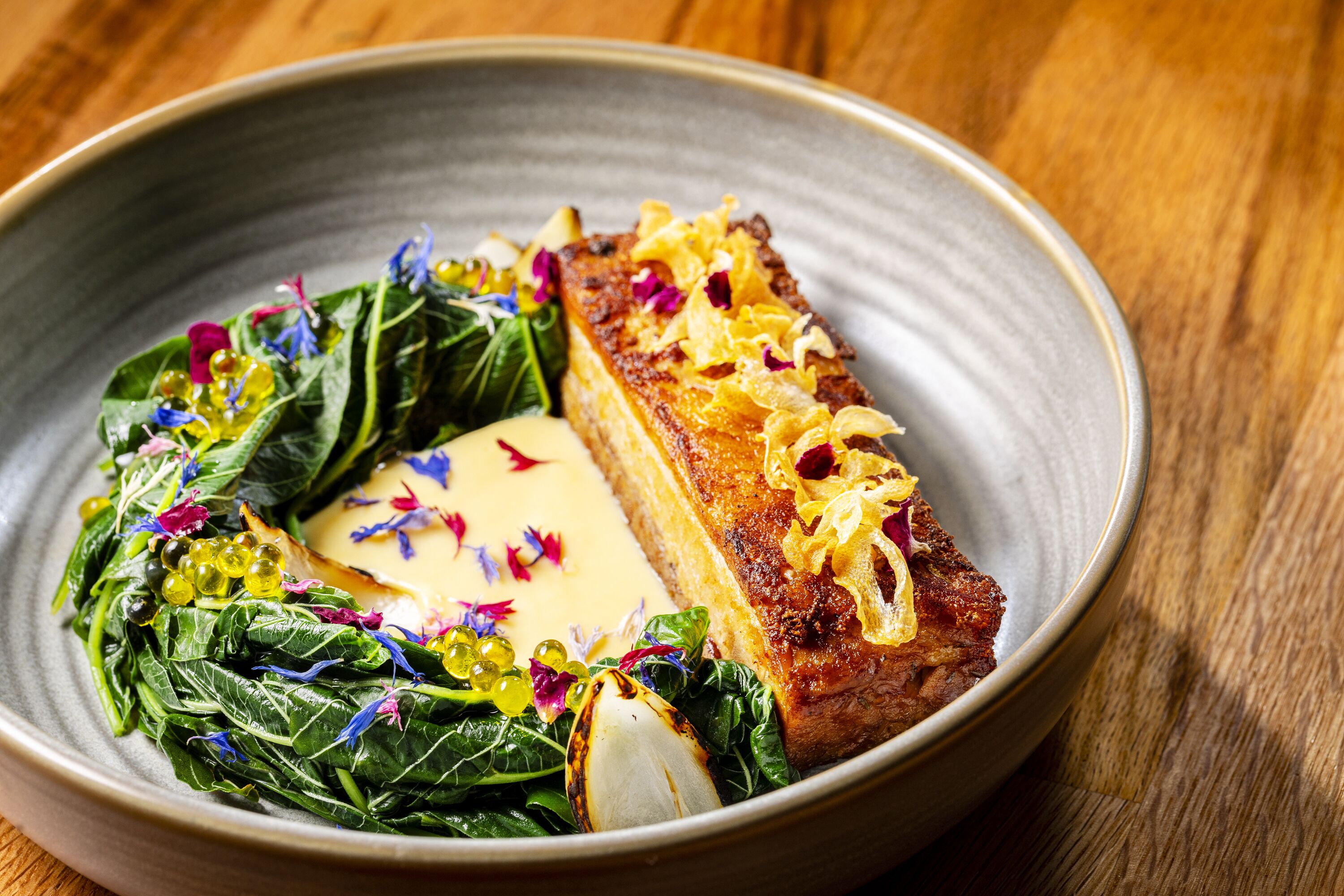 A plate with a piece of meat, greens, and a dollop of sauce.