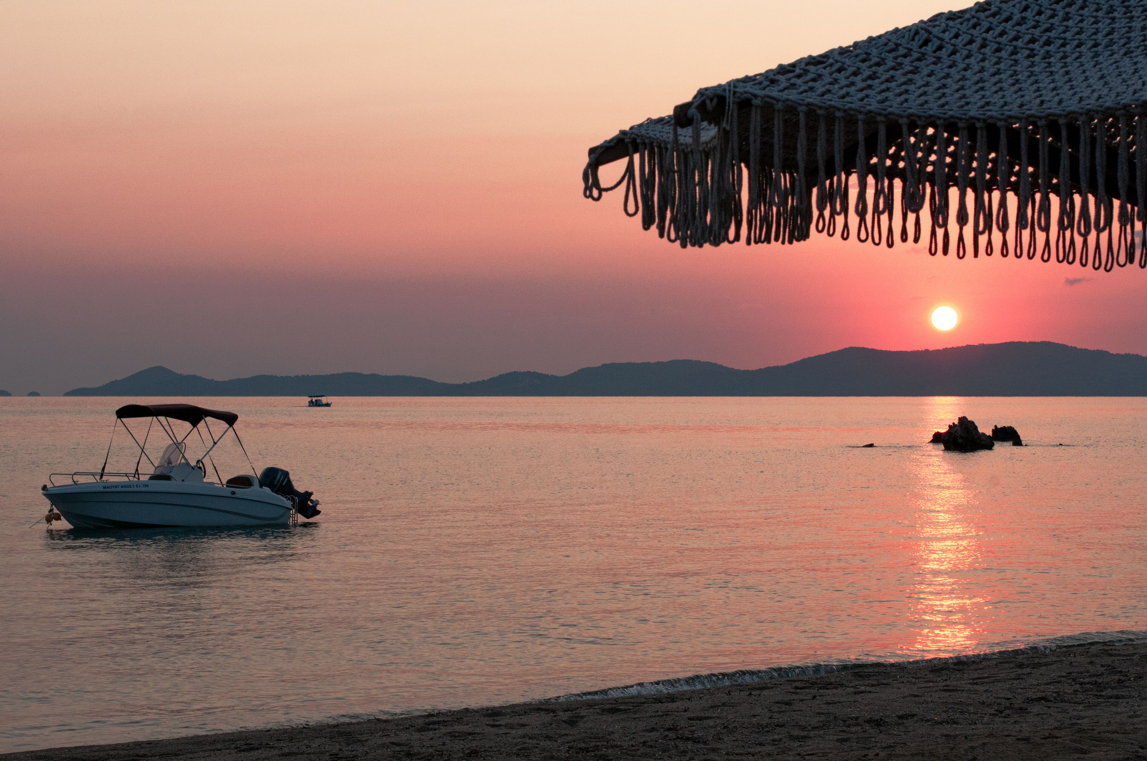 Un bote sobre aguas tranquilas durante el atardecer, una playa y montañas distantes.