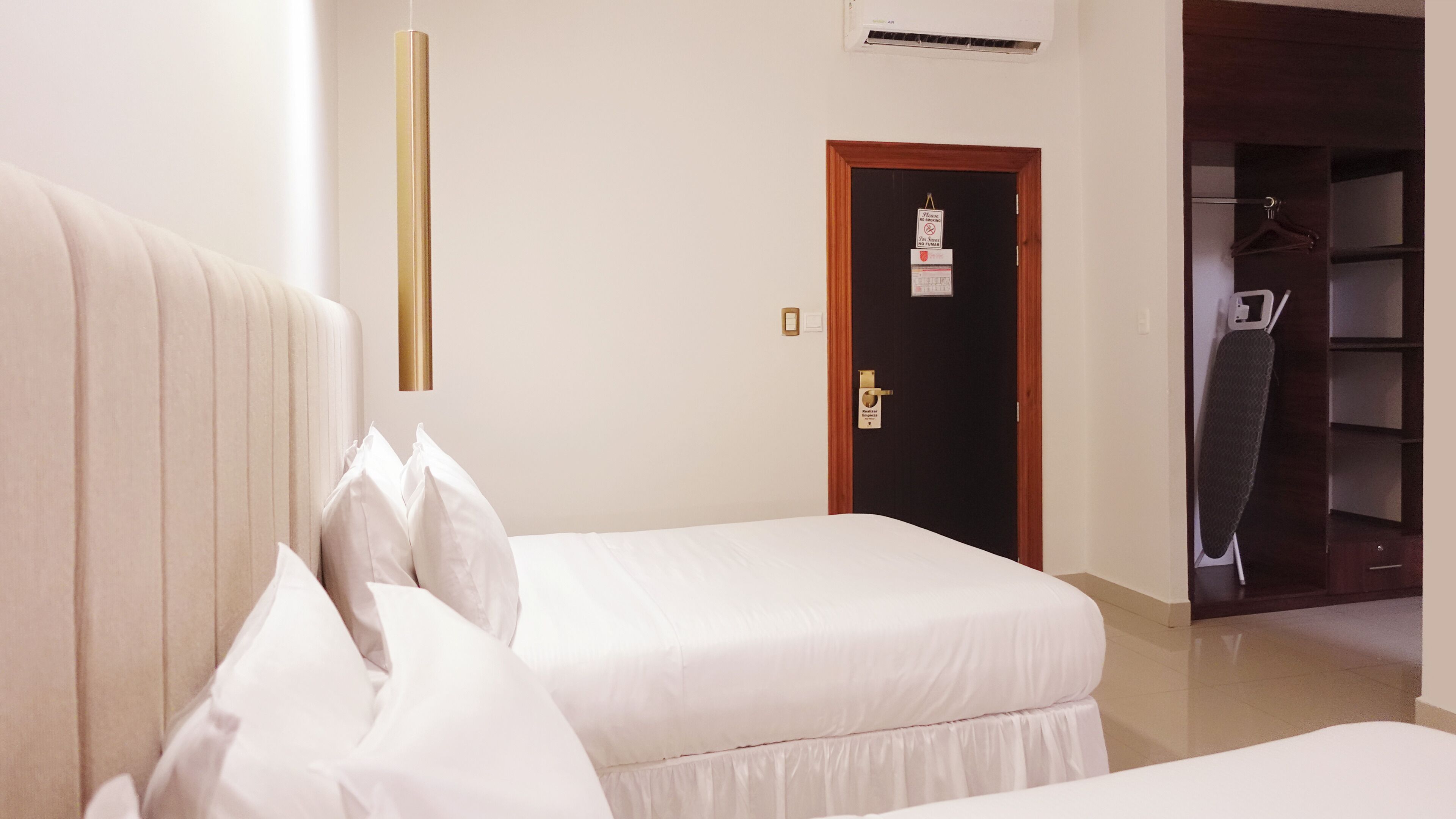 A hotel room with two beds, a wardrobe, and a door with a sign.