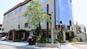 Un edificio moderno con fachada de vidrio, un árbol en primer plano y un coche rojo aparcado cerca.