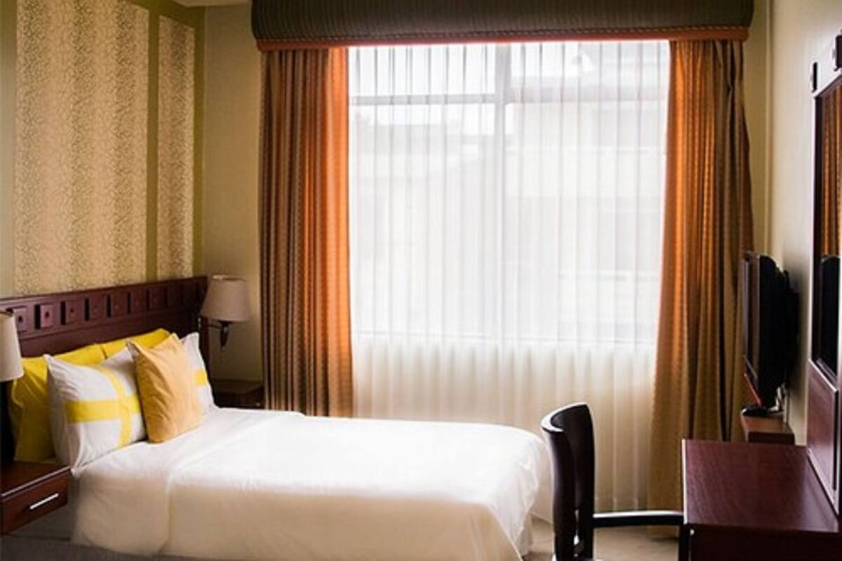 A hotel room with a bed, a desk, a chair, a TV, and a window with curtains.