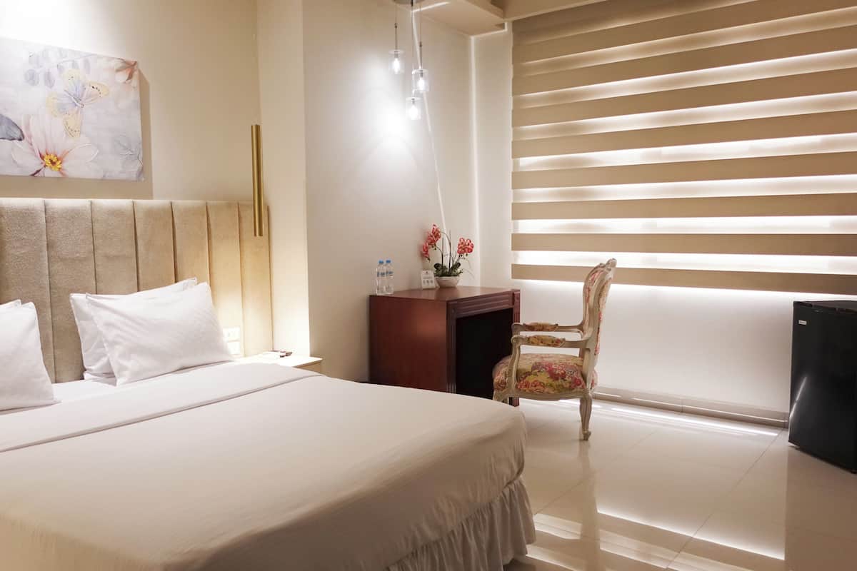 A hotel room with a bed, a desk, a chair, a water bottle, and a plant.