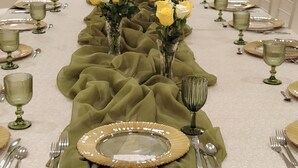 Una larga mesa de banquete con manteles verdes, copas con detalles dorados y rosas amarillas.