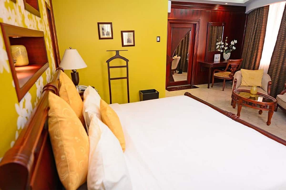 A hotel room with a large bed, a desk, a chair, a lamp, and a mirror.