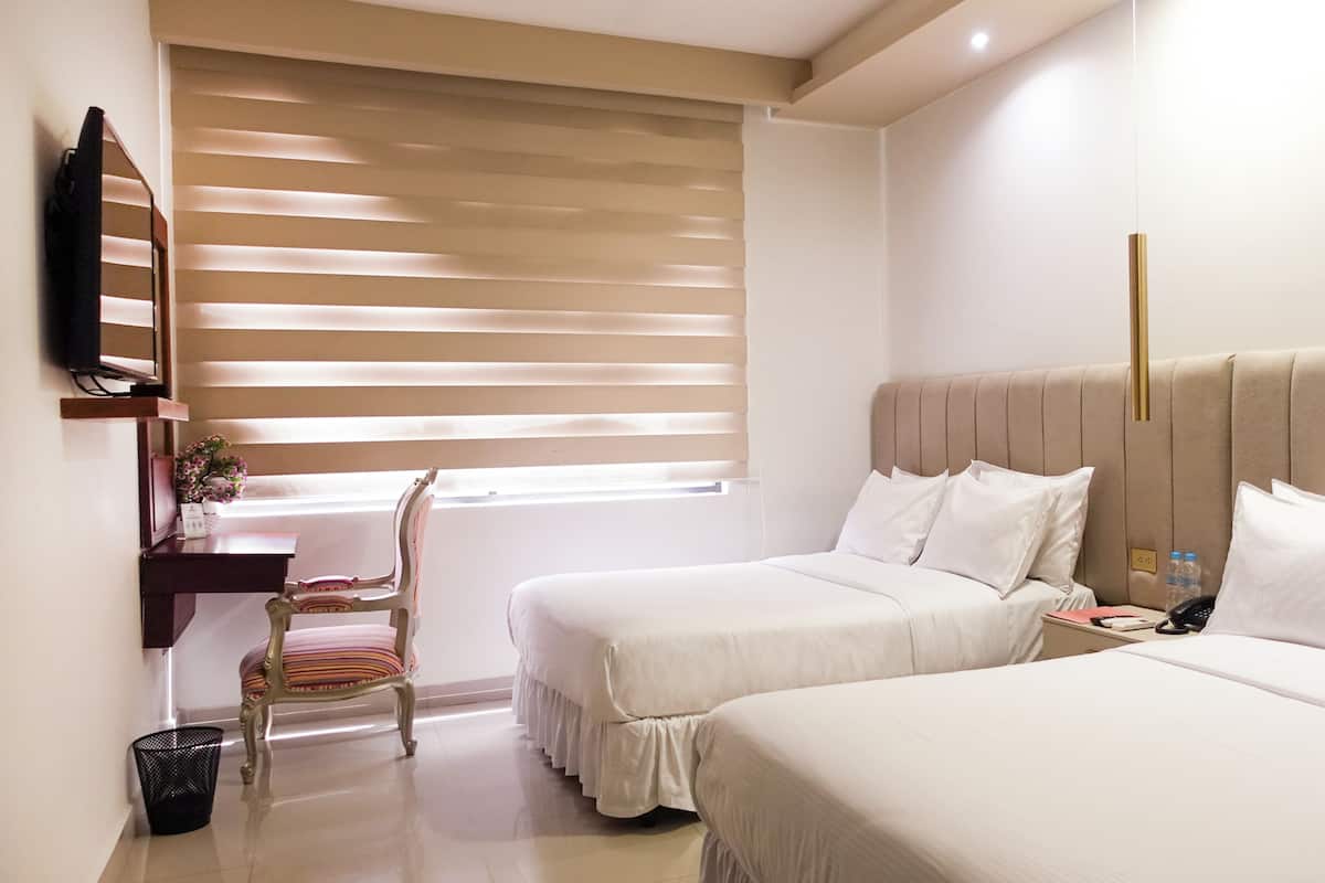 A hotel room with two beds, a desk with a chair, a TV, and a window with blinds.