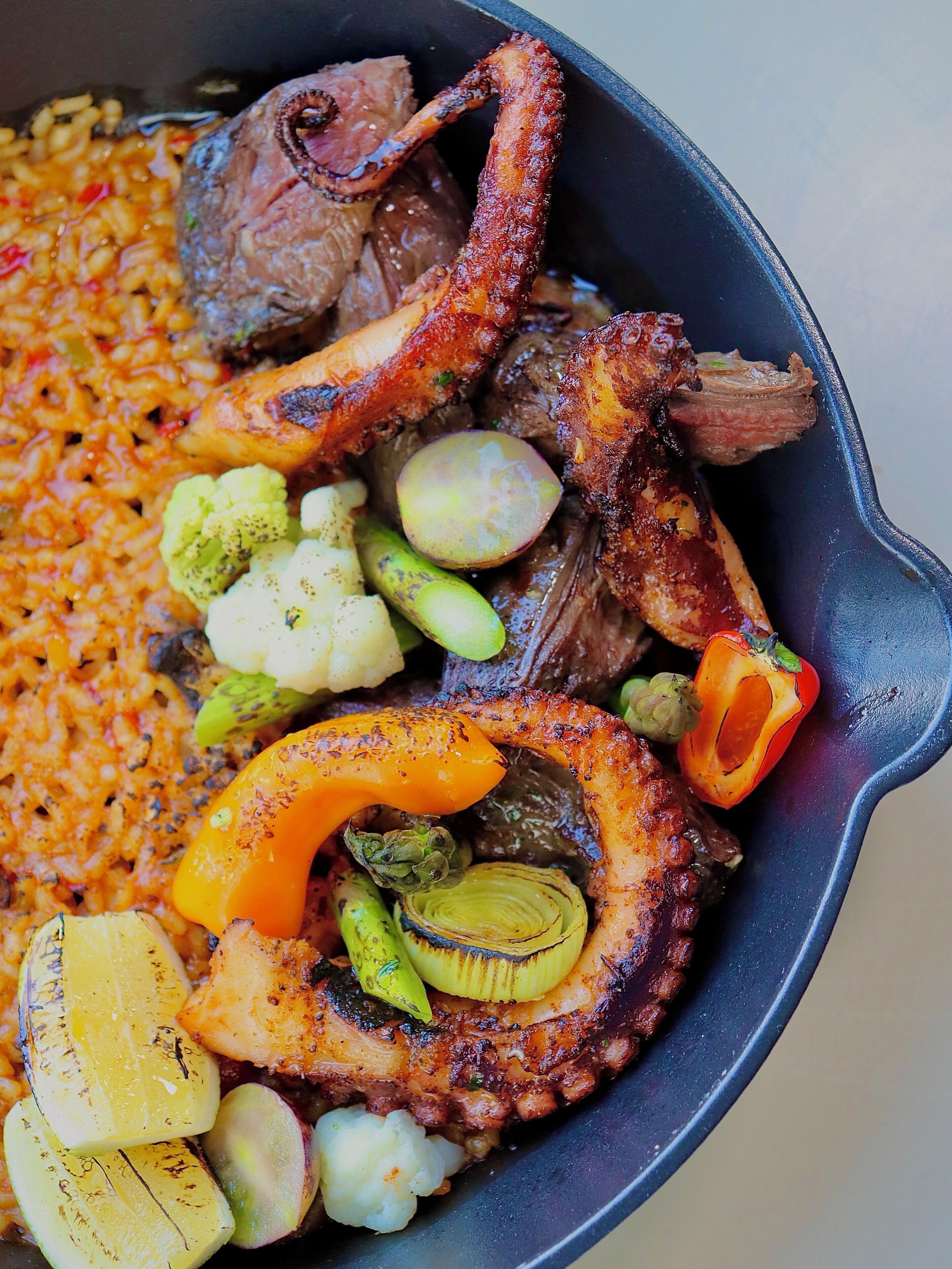 A skillet with grilled octopus, vegetables, and rice.