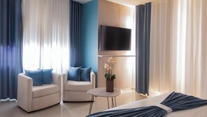 Una habitación de hotel moderna con sofá, sillón, mesita y televisor de pantalla plana en la pared.