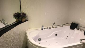 Un baño moderno con una bañera grande, un espejo y un estante con objetos decorativos.