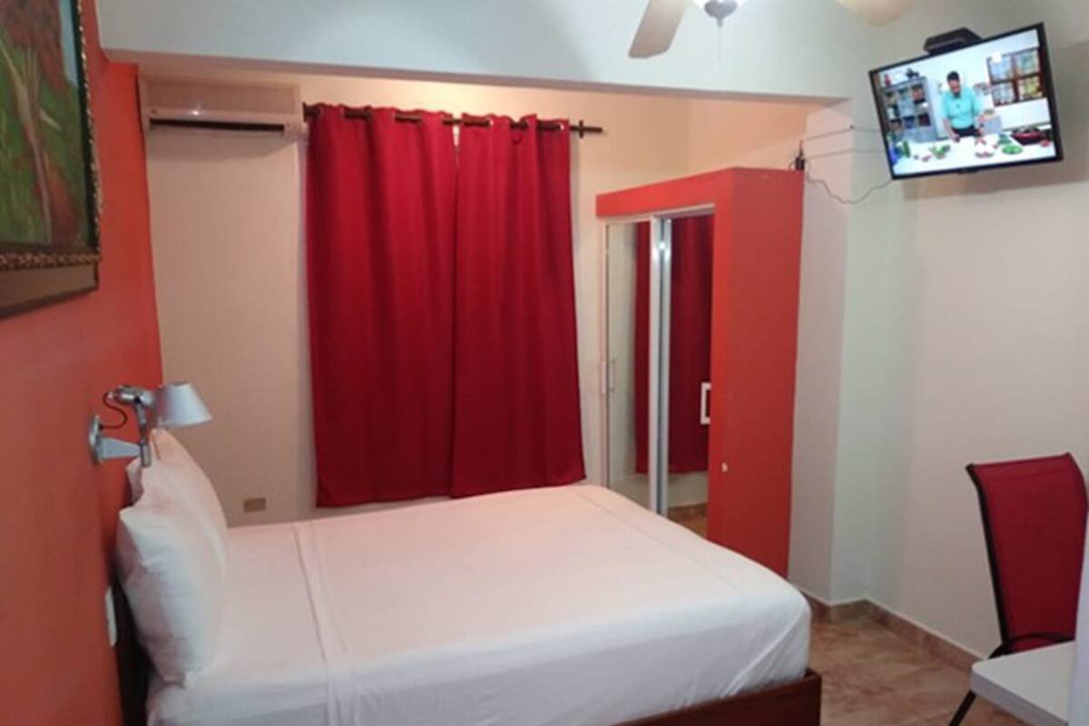 A bedroom with a bed, a TV mounted on the wall, and a red curtain.