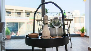A table with a bottle of JP Chenet ice wine, two wine glasses, and a bowl on a black metal stand in a room with a view of a building with a sign reading "FOB AQUARIUM SHOPPING CENTRE". - Phaedrus Living: Seaside Luxury Flat Athina 109 (Paphos)